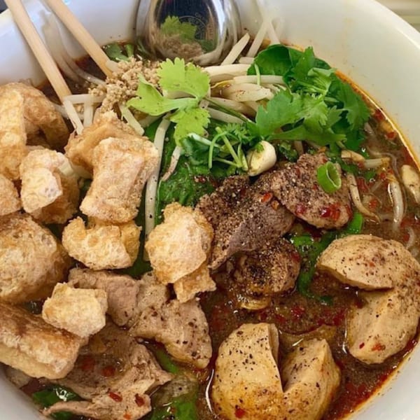 Close-up of a bowl of 9 Thai Restaurant's boat noodles with pork rinds, meatballs, and herbs.