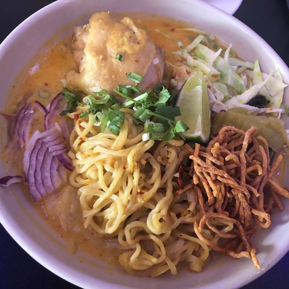 A bowl of 9 Thai Restaurant's Khao Soi with chicken, noodles, red onion, cilantro, and lime.