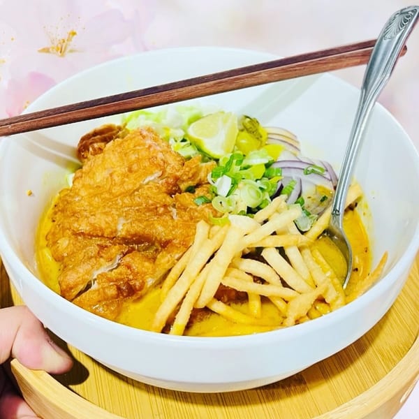 A bowl of 9 Thai Restaurant's Khao Soi with crispy chicken, noodles, and garnishes.