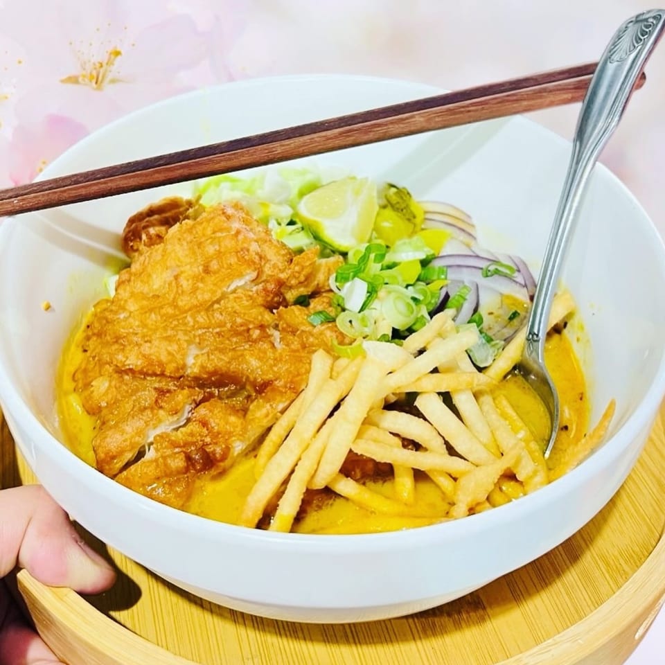 A bowl of 9 Thai Restaurant's Khao Soi with crispy chicken, noodles, and garnishes.