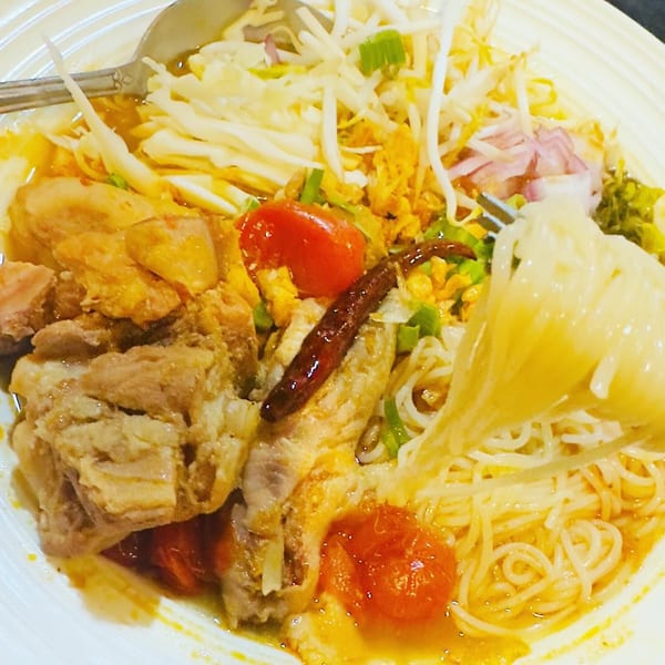 A close-up of Thai noodles with chicken, tomatoes, bean sprouts, and chili in a rich broth.