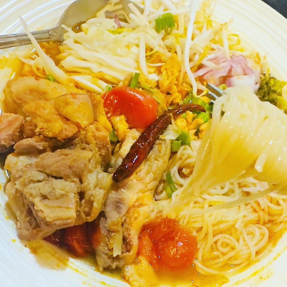 A close-up of Thai noodles with chicken, tomatoes, bean sprouts, and chili in a rich broth.
