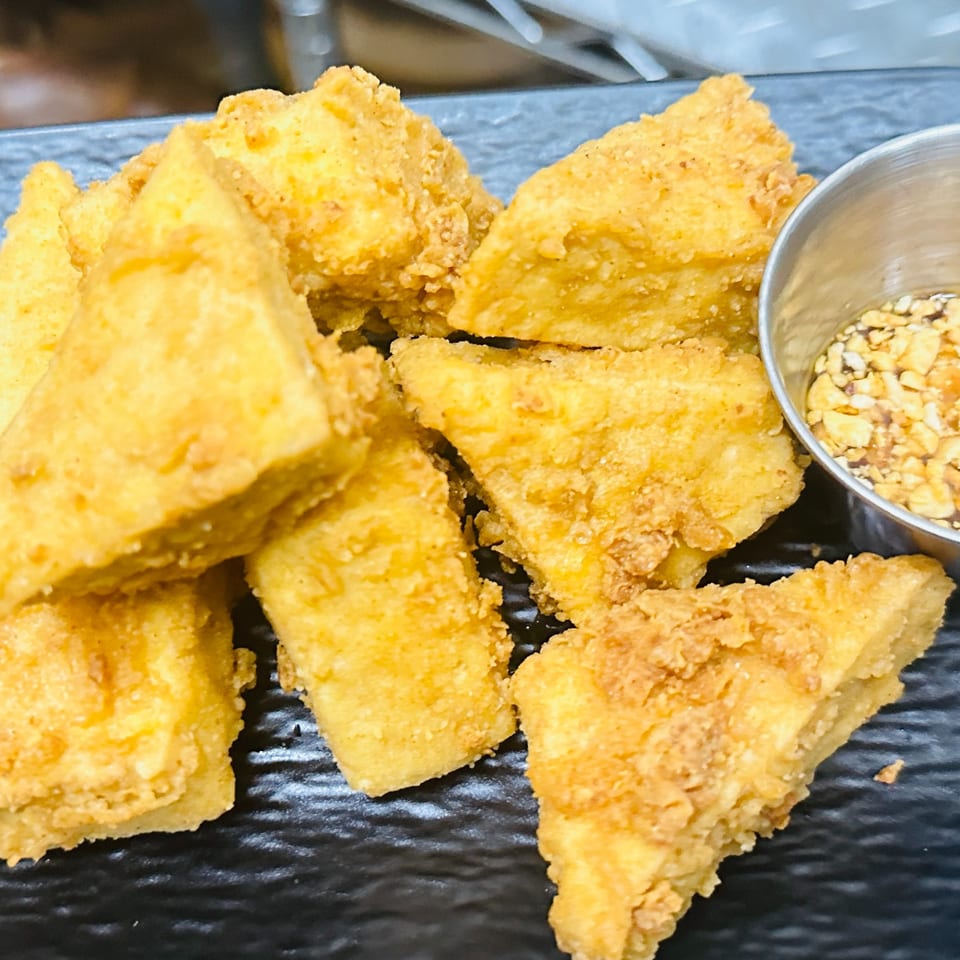 Golden fried tofu triangles with a side of dipping sauce containing crushed peanuts.