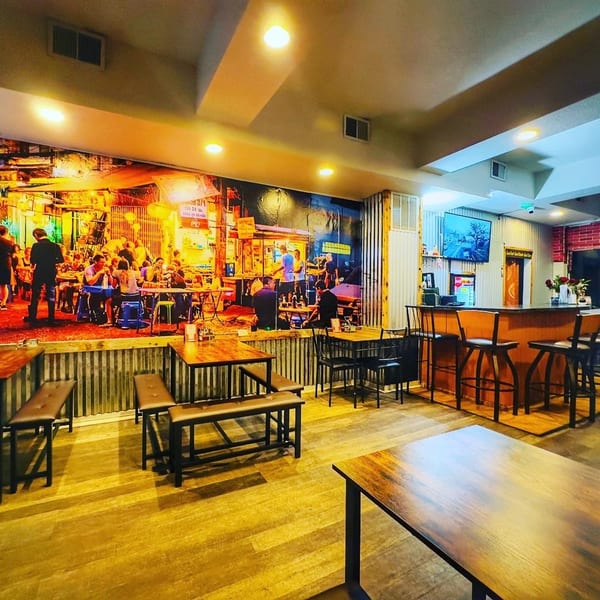 Interior of 9 Thai Restaurant with a large mural of a bustling Thai street scene, tables, and a bar.