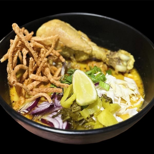 A bowl of 9 Thai Restaurant's Khao Soi with chicken leg, crispy noodles, and garnishes.